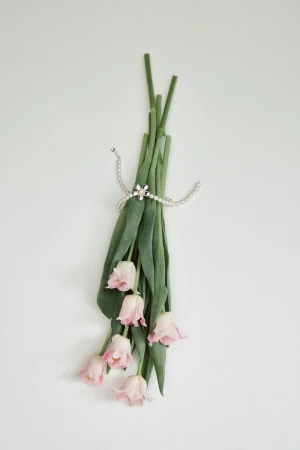 A bouquet of pink tulips tied with a pearl necklace and flower brooch against a plain white background.