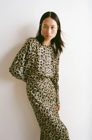 East Asian woman in a black and beige printed long-sleeve dress and large silver hoop earrings posing against a white background