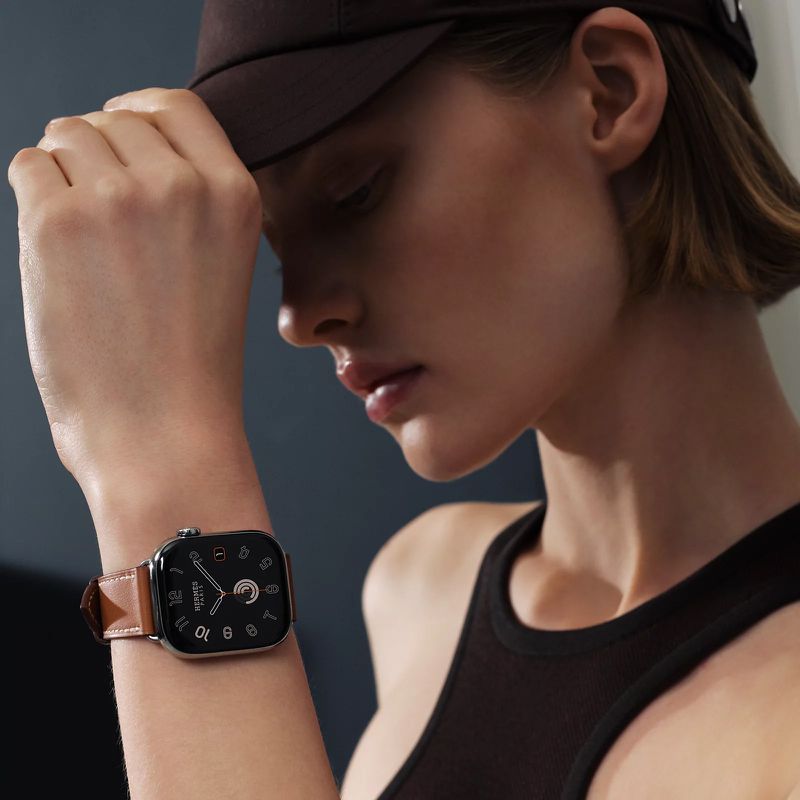 Close-up of an adult woman wearing a black tank top, cap, and a modern wristwatch with a brown leather band on her left wrist.