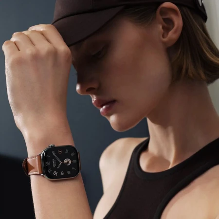 Maya Vozhdaeva wearing an Apple Watch Hermès with a brown leather strap and black cap in a studio portrait.