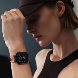 Maya Vozhdaeva wearing an Apple Watch Hermès with a brown leather strap and black cap in a studio portrait.