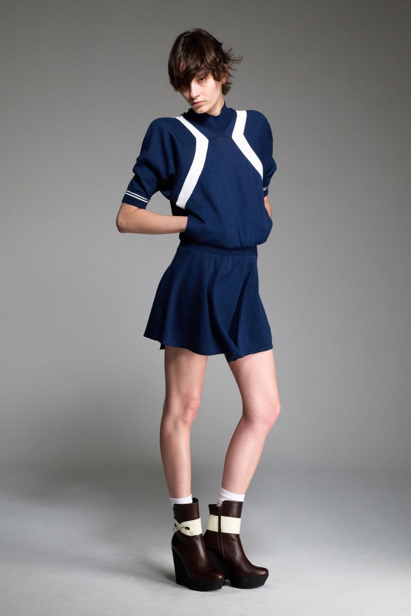 Full-length shot of a young adult female fashion model in a blue dress with white accents and dark brown platform boots, indoors.