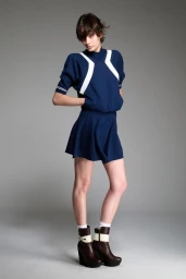 Model posing in a navy blue top with white stripes, matching blue mini skirt, and brown platform ankle boots against a grey studio backdrop.