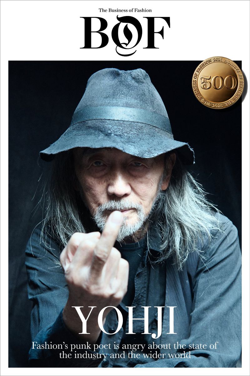 Magazine cover of Yohji Yamamoto, featuring a portrait of the fashion designer in a hat, shirt, with long gray hair, raising his middle finger.