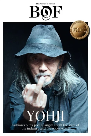 Magazine cover of Yohji Yamamoto, featuring a portrait of the fashion designer in a hat, shirt, with long gray hair, raising his middle finger.
