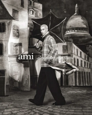 An adult male model poses with an umbrella in a faux painted-style backdrop resembling a city street, in a black-and-white artistic shot.