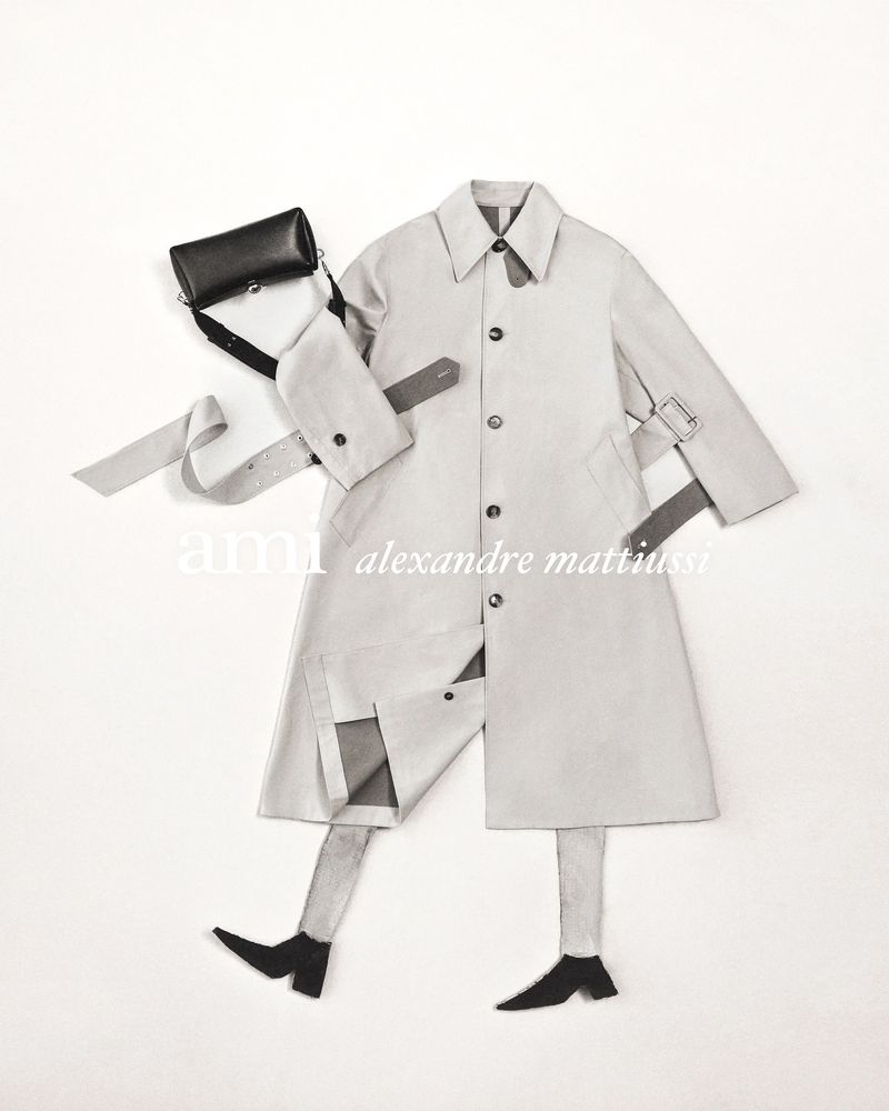 Fashion editorial featuring a beige trench coat laid flat on a white surface with a black cross-body bag and leg cutouts suggesting a person.