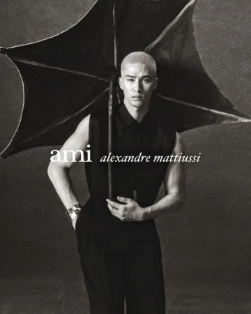 Monochrome fashion portrait of a man holding a black umbrella wearing a sleeveless black top against a dark textured background.