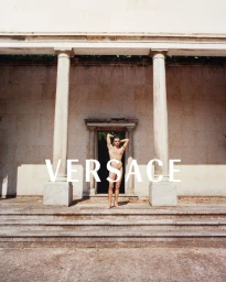 Primo Torreiro posing nude centered between classical stone columns with white Versace typography overlay.