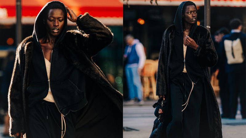 Fashionable person in fur coat and dark hooded jacket, stands on city street with blurred pedestrians in the background. Fashion shot.