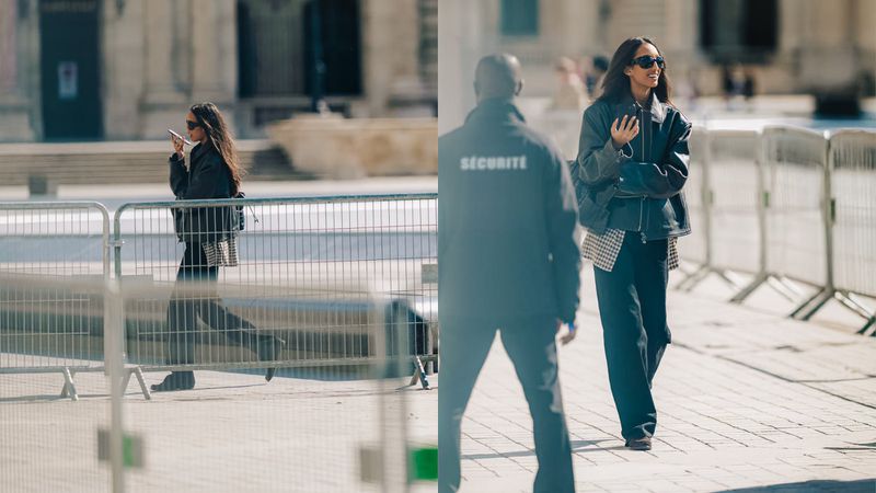 Two women walk on a plaza in leather jackets and sunglasses with a security guard partially blocking the view, creating a street-style fashion moment.