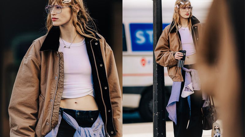 A woman with glasses and hair clips poses in a crop top and jacket in a street style fashion shoot with a blurred background.