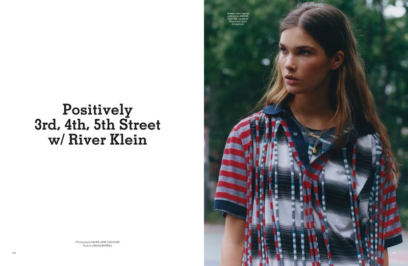 Editorial fashion shot: A young woman in a plaid top poses outdoors with soft, natural lighting and a blurred background of trees.