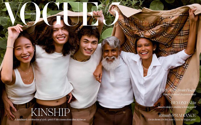 Vogue Singapore cover with a diverse group of five people smiling, huddling under a Burberry trench coat outside among green foliage.