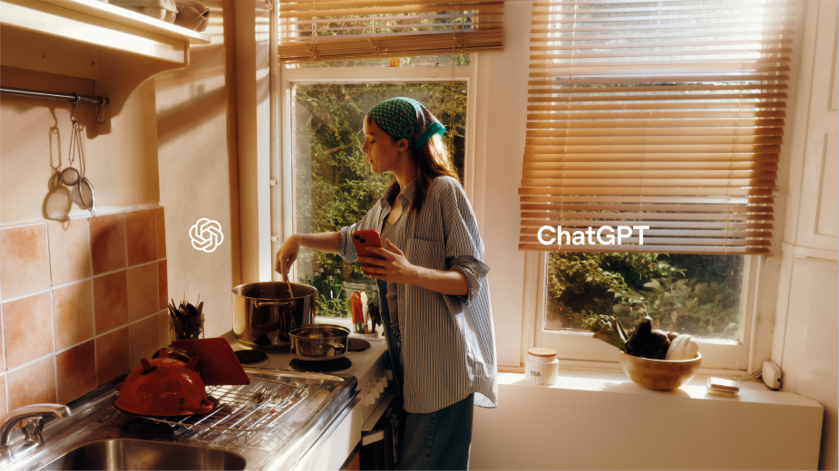 Woman cooking in a brightly lit kitchen, stirring a pot while holding a phone, with natural light streaming through the window and text overlay.
