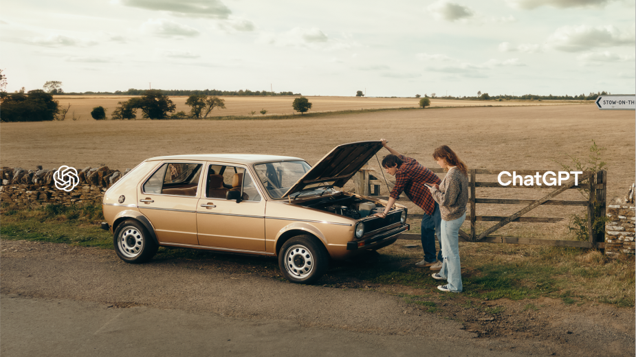 Tan car on roadside with hood open as two adults look at engine. Rural setting with field and fence. OpenAI ChatGPT logo.