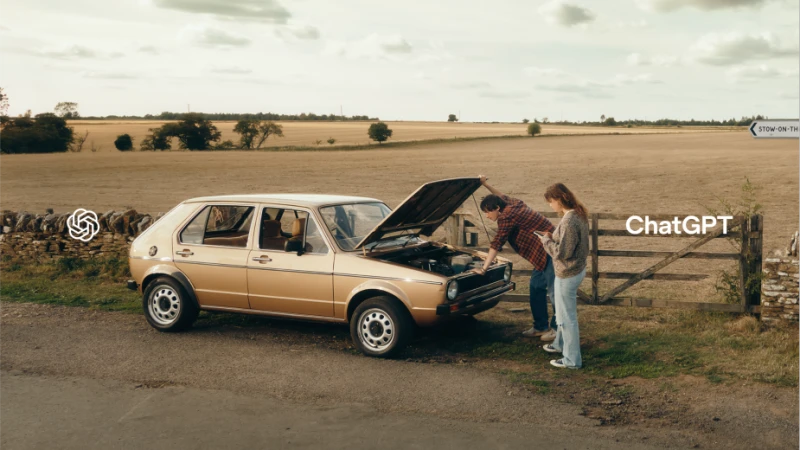 Tan car on roadside with hood open as two adults look at engine. Rural setting with field and fence. OpenAI ChatGPT logo.