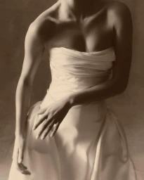Close-up portrait of a model wearing a structured white strapless gown with draped bodice against a muted neutral background.