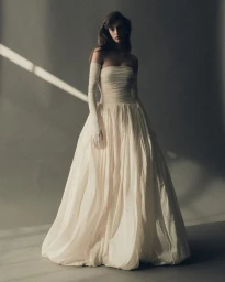 A model wearing a strapless ivory gown with matching opera gloves against a grey studio backdrop.