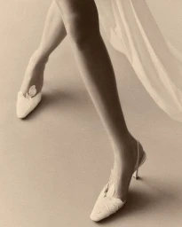 Close-up shot of model legs wearing white slingback heels against a neutral studio backdrop for Danielle Frankel.