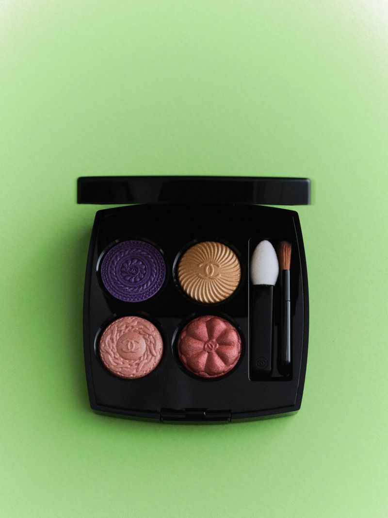 Chanel eye shadow palette in a black compact with four colors and applicator brushes, set against a light green background.