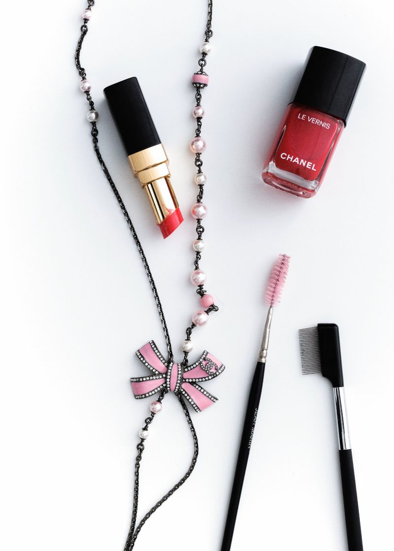Beauty still life: Lipstick, nail polish, necklace, and makeup brushes on a white surface, showcasing beauty and cosmetic products.