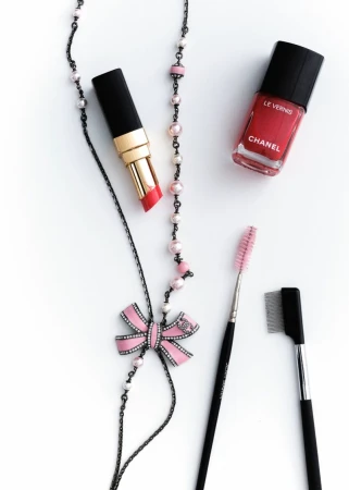 Beauty still life: Lipstick, nail polish, necklace, and makeup brushes on a white surface, showcasing beauty and cosmetic products.