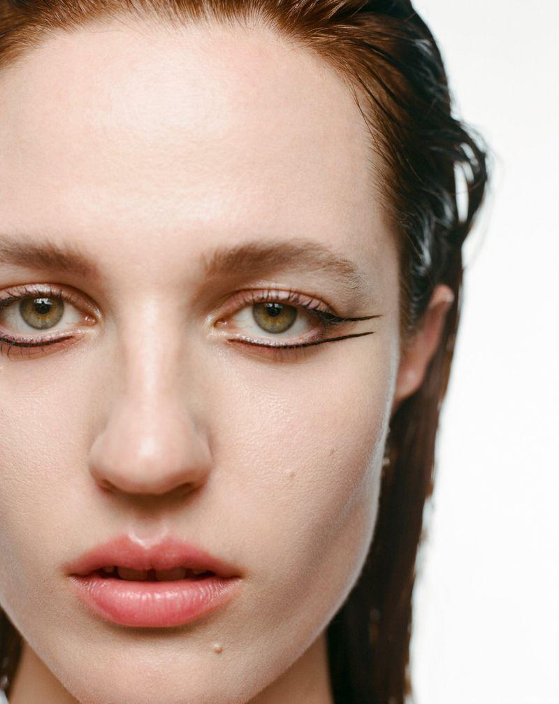 Close-up portrait of a fair-skinned woman with dark hair and eyeliner, gazing at the camera against a clean white background.