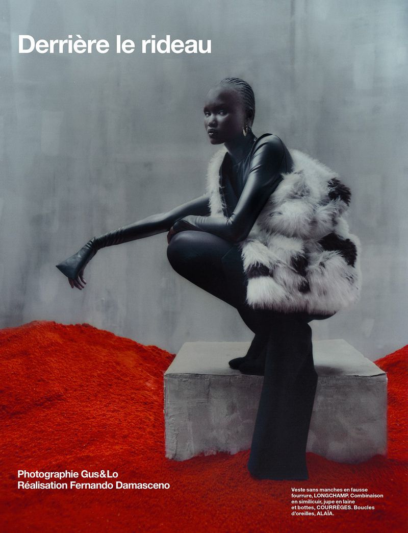 Fashion editorial shot of a woman in black clothing and a faux fur vest posing on a concrete block with red fur carpet.