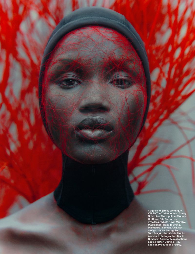 Close-up studio portrait of a dark-skinned woman wearing a black head covering, with red network-like lines overlaying her face and body.