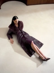 Model wearing a dark leather coat with a furry collar lying on a pale floor for Nour Hammour
