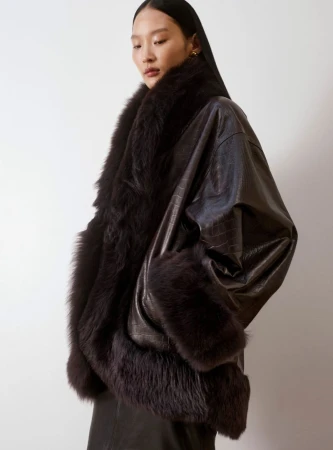 Brunette Asian model showcases a dark brown, textured, oversized jacket trimmed with dark fur against a plain background in a studio shot.
