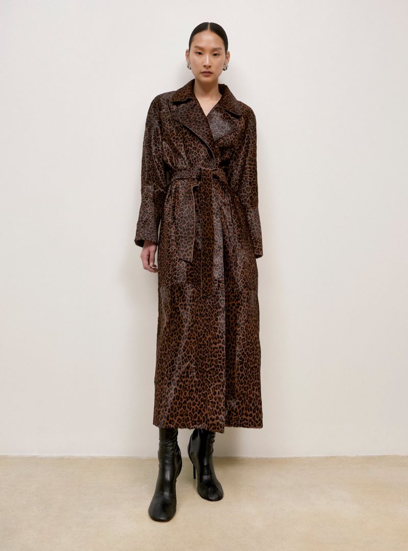 Full-length shot of a stylish Asian woman wearing a brown leopard print trench coat, black heeled boots in a neutral indoor setting.