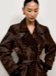 Model wearing a dark patterned belted coat with motion blur against a neutral background for Nour Hammour Fall Winter 25