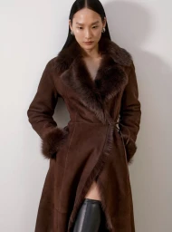 Model wearing a brown belted coat with fur collar against a white background