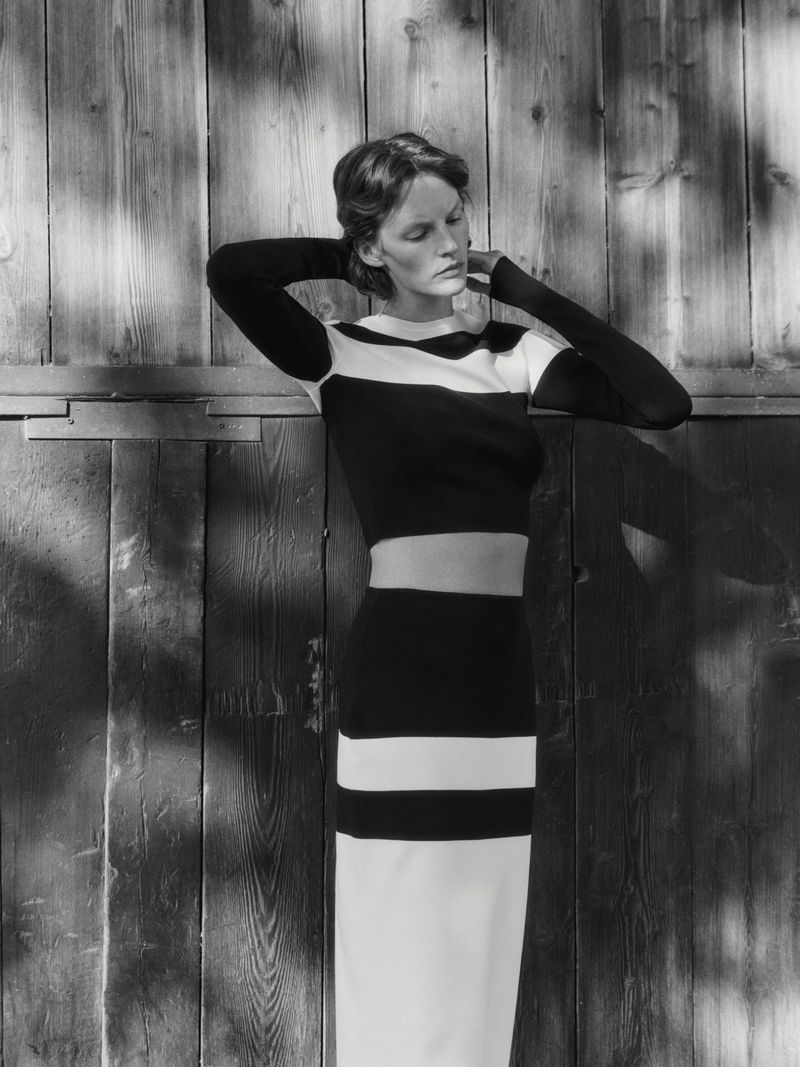 Monochrome portrait of a woman in a black and white striped knit outfit against a wooden background with shadow patterns.