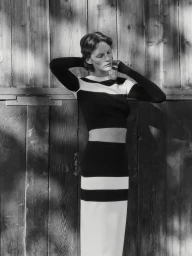 Model wearing a black and white striped top and matching skirt standing in front of a vertical wooden plank wall