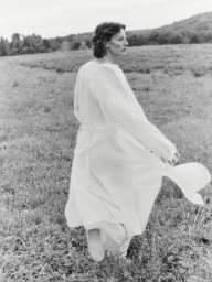 Model Sara Blomqvist wearing a white belted coat walking through an open meadow for Giada 2025 SS Leisure