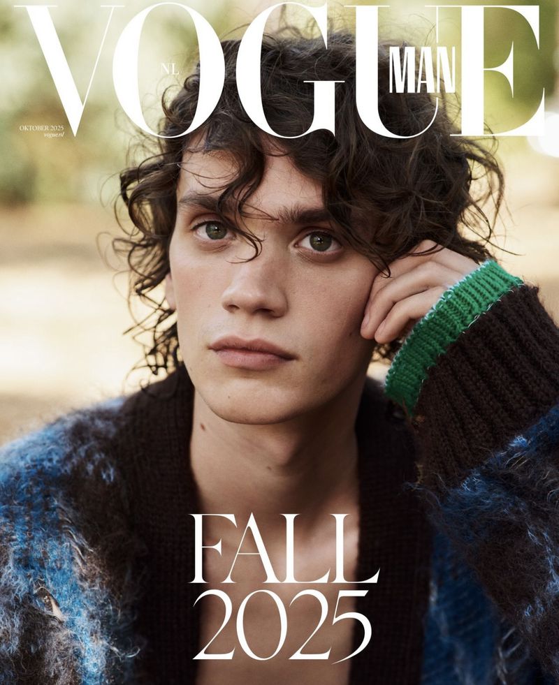 Vogue Man cover featuring a portrait of a young adult male with curly brown hair and a blue and black cardigan, shot outdoors with autumn foliage.