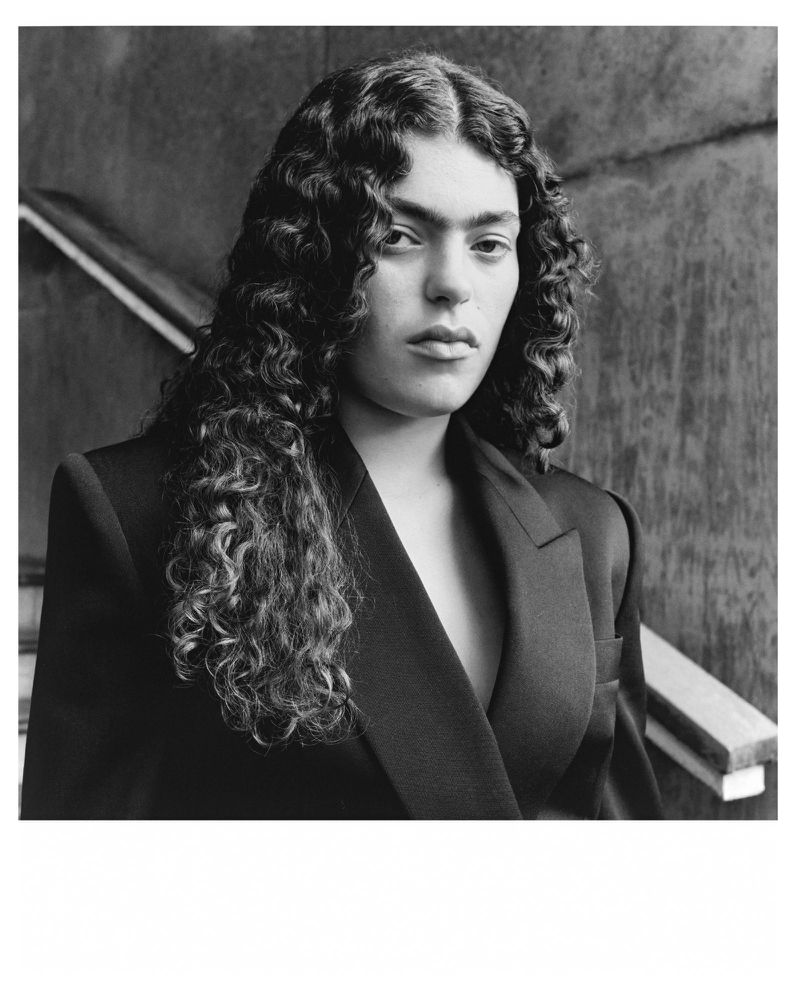 Black and white portrait of an adult with curly hair wearing a blazer. Studio shot with soft lighting and shallow depth of field.