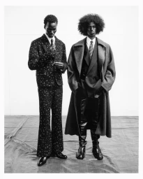 Two Black male models in tailored menswear and long overcoats standing in a studio for Dazed MENA Issue 03.