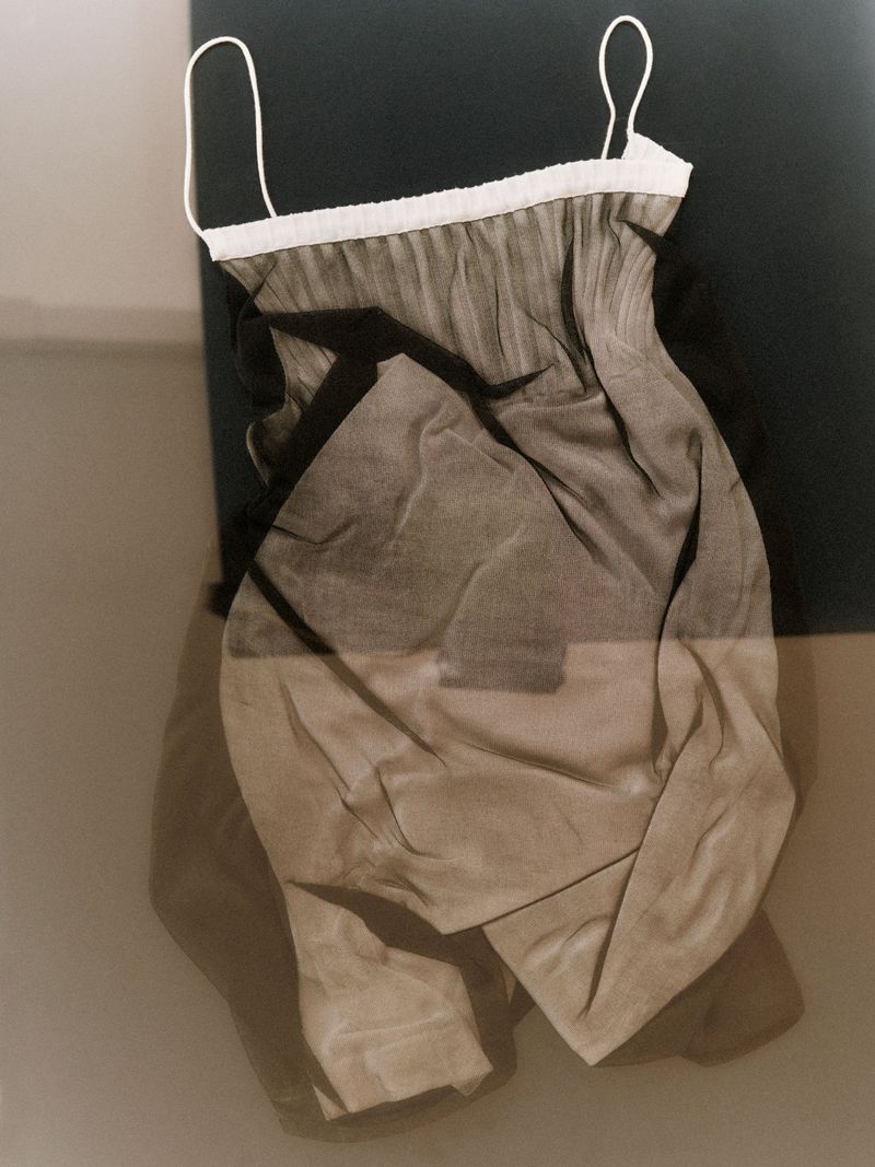 A black and beige sheer negligee with white trim and spaghetti straps is displayed against a gray backdrop in a studio setting.