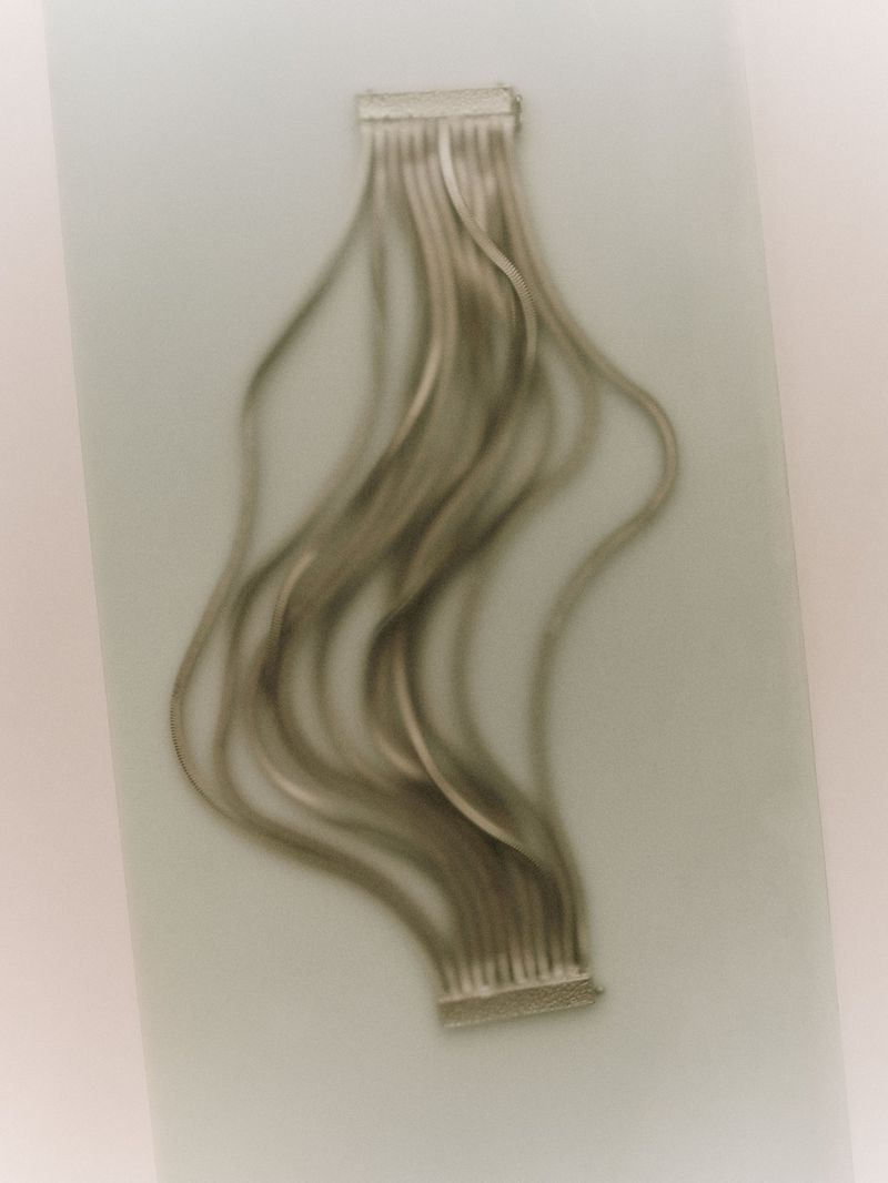 Close-up of silver hair extensions with wavy strands attached to clips, displayed against a muted background, beauty concept.