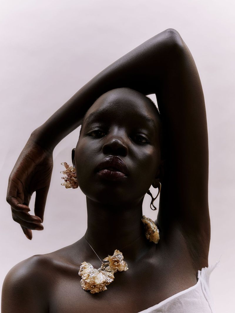 Close-up of a dark-skinned woman wearing an ornamental necklace and earrings, posing in a studio with soft, diffused lighting.