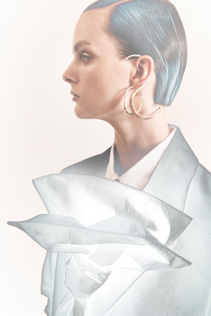 Fashion portrait of a female model in a light blue blazer with oversized earrings, showcasing a sleek, modern aesthetic.