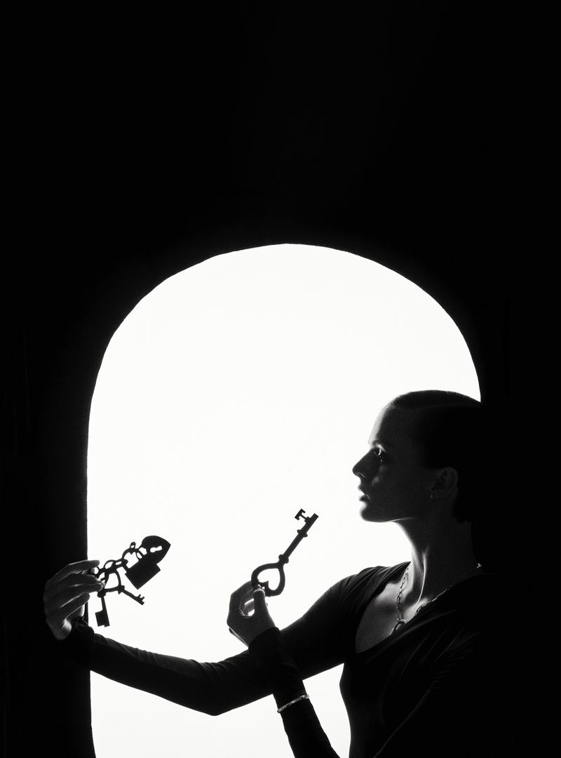 Silhouette of a woman holding a heart-shaped key and padlocks against a bright background, creating a contrasting light and shadow image.