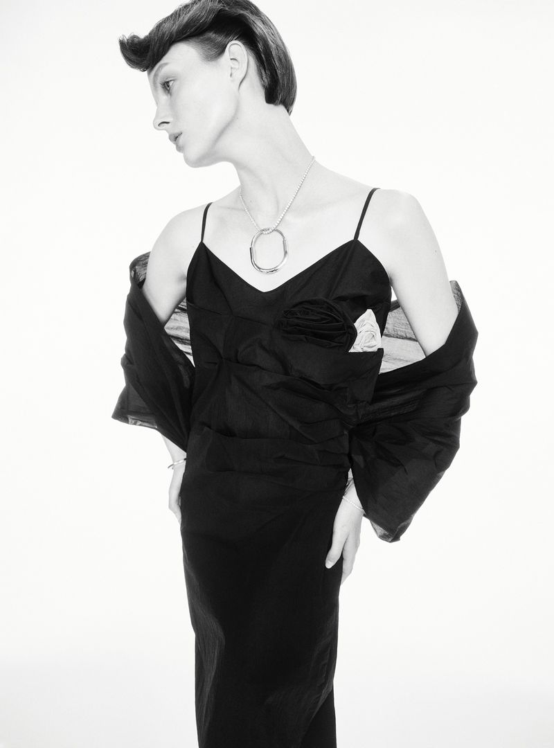 Elegant fashion portrait of a slim adult woman in a black dress with silver necklace on a white background in a photo studio.