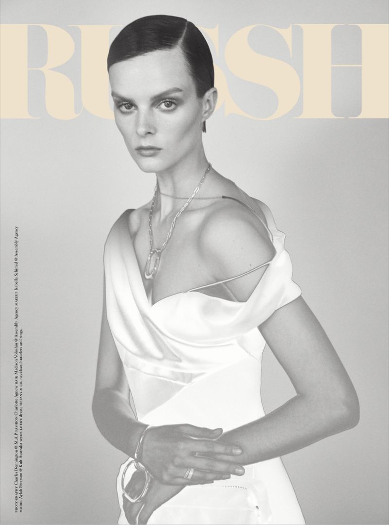 Fashion magazine cover featuring a model with short dark hair, wearing a white off-shoulder dress and silver jewelry, against a light background.