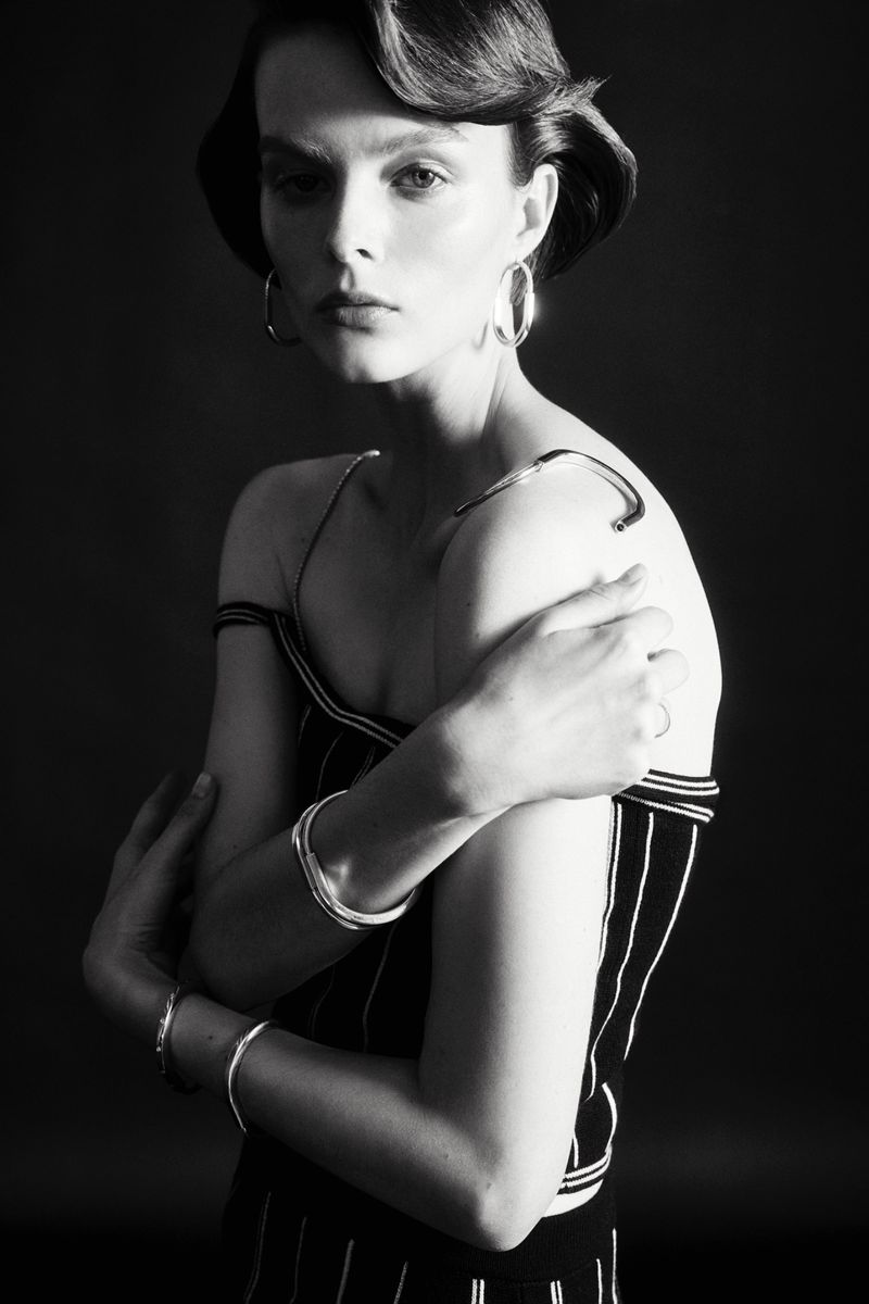 Black-and-white portrait of a woman with dark hair, wearing a striped top and silver hoop earrings, posing in a studio with a dark background.