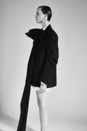 Profile view of a model in a black blazer with an elongated tie against a plain light background